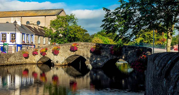 Stenen brug met bloemen over een rivier, omringd door gebouwen.