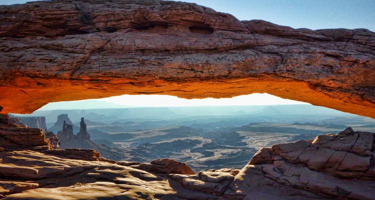Sunrise light glows beneath Mesa Arch framing a vast canyon landscape.