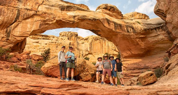 Group of travelers smiling beneath a natural sandstone arch with golden rock walls around them.