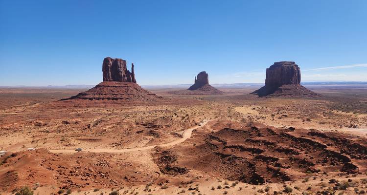 Large panorama désertique de Monument Valley avec les célèbres Mittens et Merrick Butte sous un ciel dégagé.
