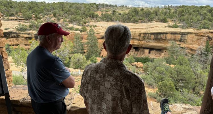 Deux voyageurs âgés contemplent les habitations troglodytiques sculptées dans les parois du canyon de Mesa Verde.