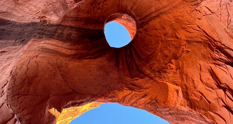Un trou circulaire dans une arche imposante de grès rouge encadre un pan de ciel bleu.