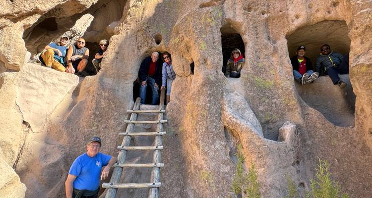 Les visiteurs grimpent une échelle en bois pour accéder aux habitations troglodytiques creusées dans le tuf volcanique avec de multiples ouvertures de grottes.