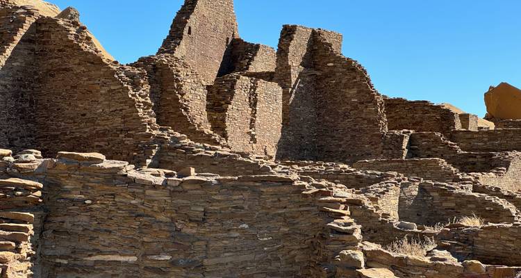 Stone ruins of massive Chacoan great house walls against a bright blue sky.