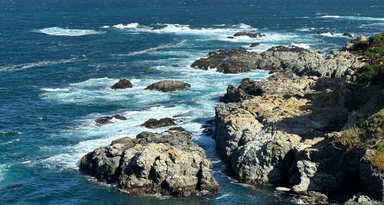 Les vagues s'écrasent contre des falaises rocheuses et escarpées le long d'un littoral d'un bleu profond.