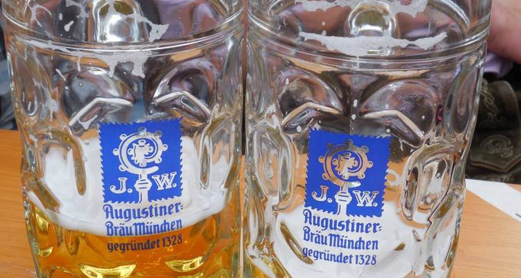 Deux chopes de bière presque vides portant le logo Augustiner Bräu München sur une table en bois.