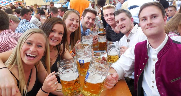 Une table de jeunes adultes joyeux en tenue traditionnelle bavaroise trinquant avec de grandes chopes de bière dans une brasserie.