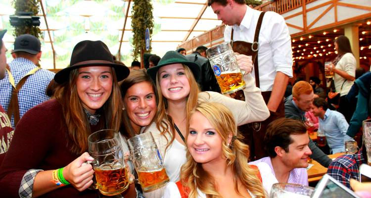 Des amis vêtus de tenues d'Oktoberfest levant des chopes de bière dans une tente de festival animée.