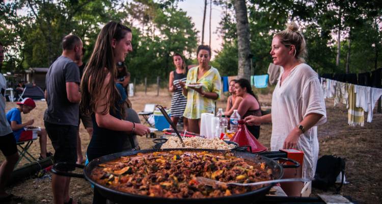 Un groupe de personnes savourant un repas en plein air avec de grandes poêles à paella.
