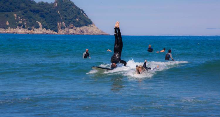 Des gens qui font du surf et nagent dans l'océan avec un littoral vallonné en arrière-plan.