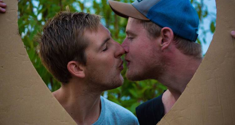 Two men framed by a cardboard cutout, about to kiss