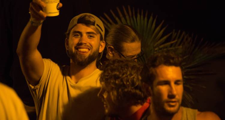 Group of friends at night, one raising a cup, dark background.