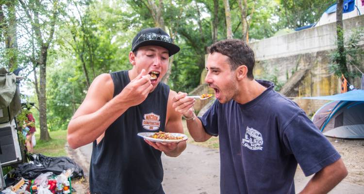 Two men eating food outdoors near tents