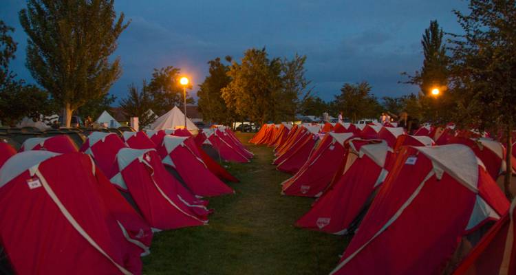 Rows of red tents set up in a grassy area at dusk