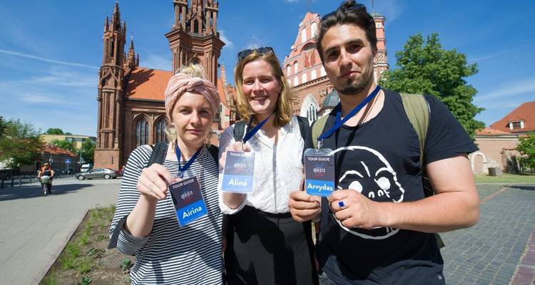 Trois personnes portant des badges de visite posent devant une église ornée.