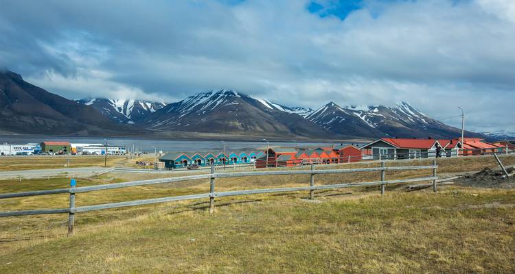 Les cabines colorées d'un établissement arctique avec en arrière-plan des montagnes enneigées et un fjord.