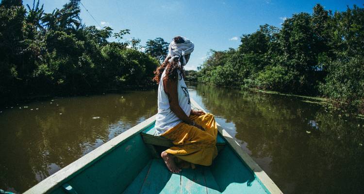 Woman sitting on a boat in a river surrounded by jungle.