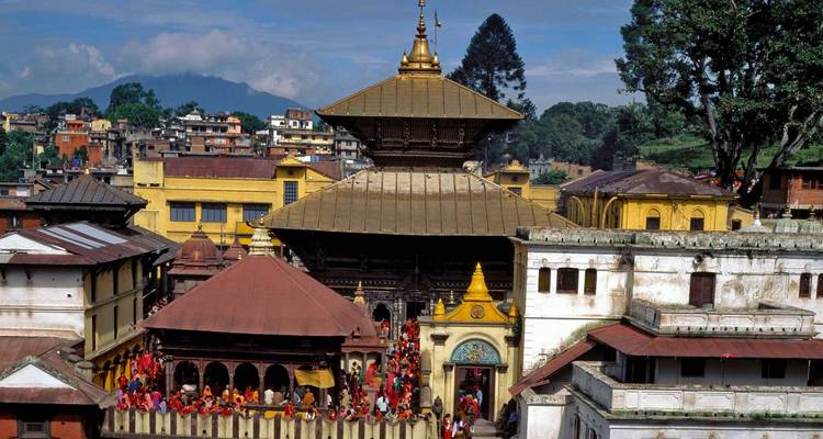 Un complexe de temples avec des gens, entouré de verdure et d'un arrière-plan montagneux.