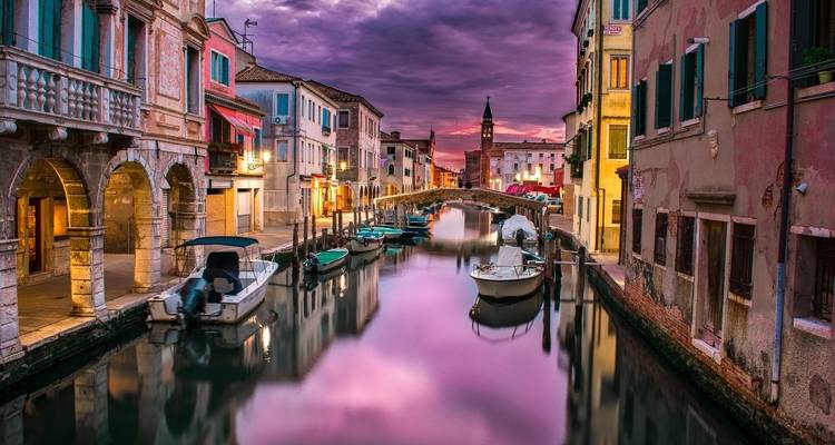 Picturesque canal scene at sunset with boats and historic buildings.