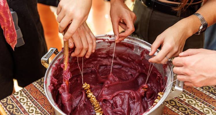 Varias manos sumergen nueces ensartadas en mosto espeso de uva para crear dulces churchkhela