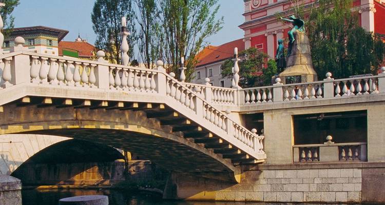 Puente con balaustrada de piedra y estatua que cruza el río Ljubljanica con edificios coloridos en Liubliana.
