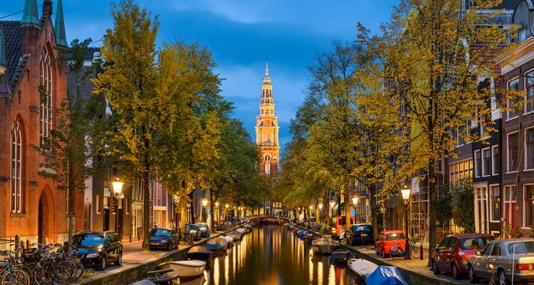 Amsterdam canal at night with a view of buildings and a church.