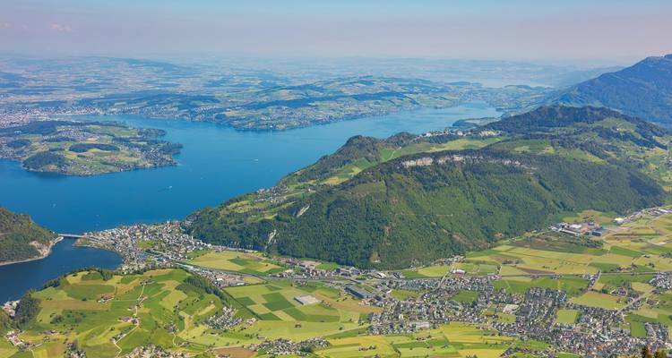 Aerial view of a large lake with surrounding green mountains and towns.