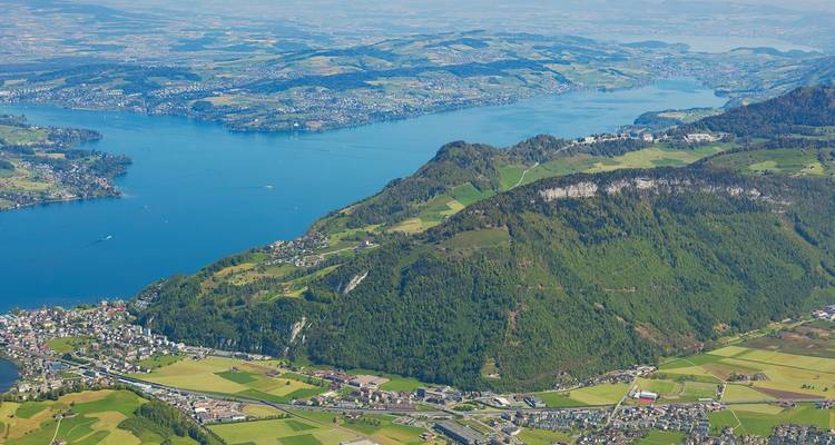 Vista aérea elevada de un lago azul profundo serpenteando entre colinas verdes exuberantes y pueblos rurales.