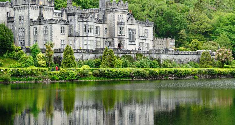 La Abadía Neogótica de Kylemore reflejada en un lago tranquilo rodeado de exuberante vegetación irlandesa.