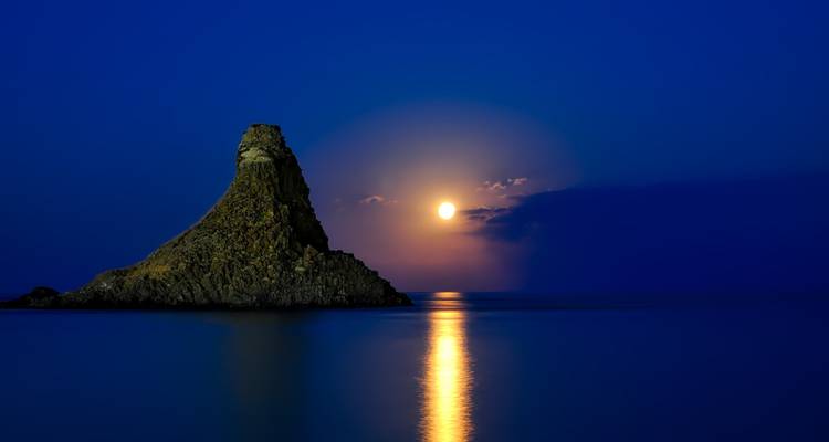 Paysage marin serein d'un îlot rocheux sous une pleine lune se reflétant sur des eaux calmes.