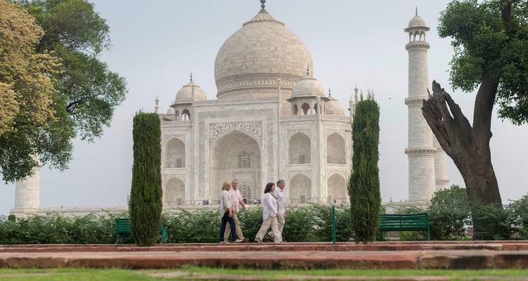 Drei Touristen spazieren in den Gärten vor dem ikonischen weißen Marmor-Mausoleum Taj Mahal.