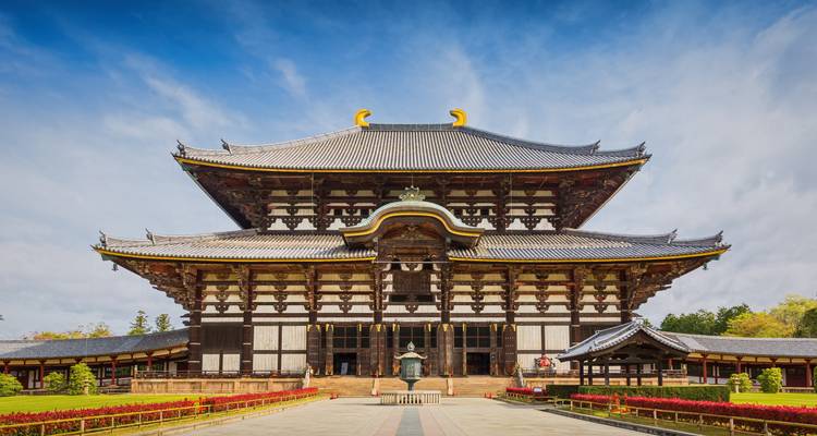 Groots houten Todai-ji tempel met symmetrische vleugels en blauwe lucht achtergrond omlijst door nette tuinen.