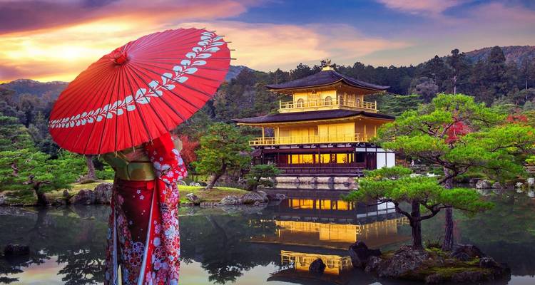 Femme vêtue d'un kimono avec un parapluie rouge contemplant le temple doré Kinkaku-ji de Kyoto reflété dans un étang au coucher du soleil.
