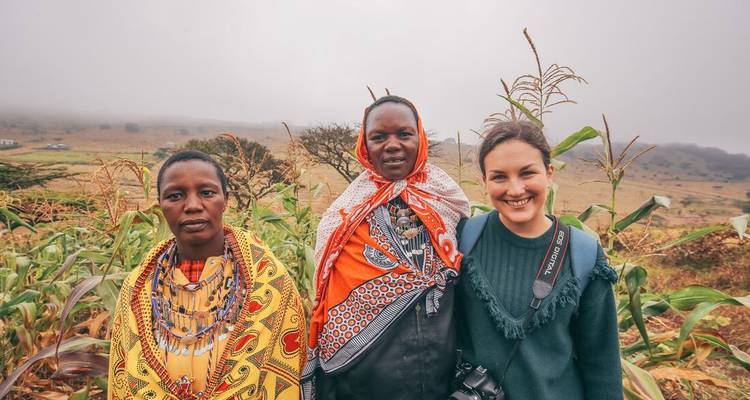 Deux femmes Maasai et un voyageur souriants ensemble dans les terres agricoles des hauts plateaux brumeux