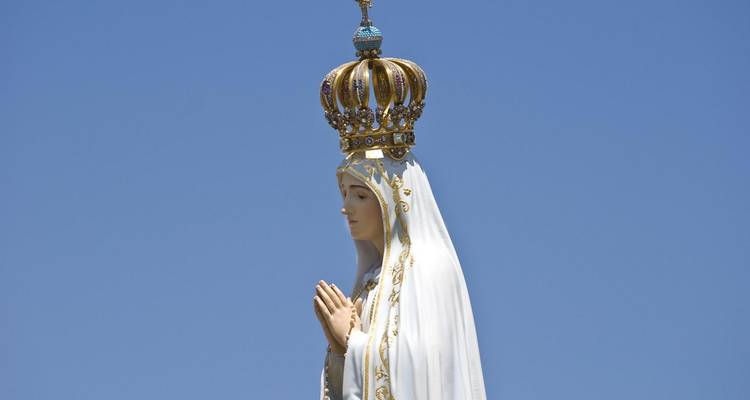 Statue einer gekrönten Figur vor einem klaren blauen Himmel.