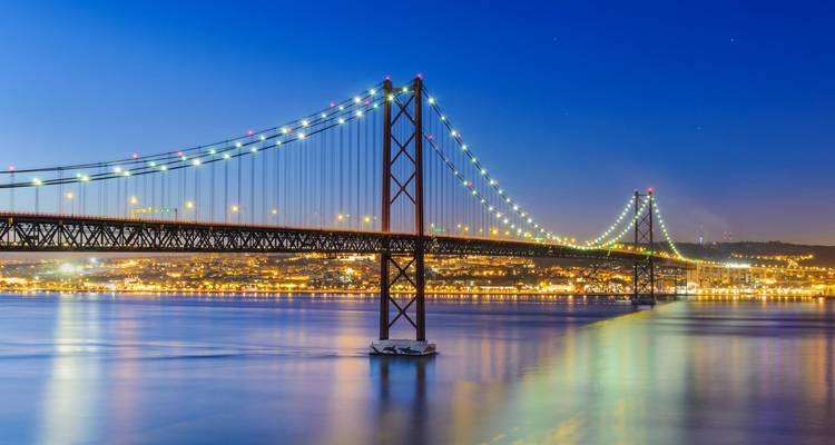Verlichte hangbrug over water bij nacht.