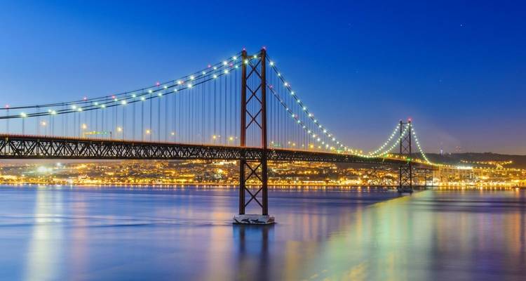 Brug verlicht 's nachts over een rivier in Lissabon.