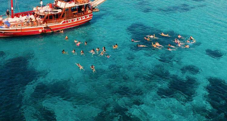 Kristalhelder Egeïsche wateren vol met snorkelaars naast een rode toeristenboot.