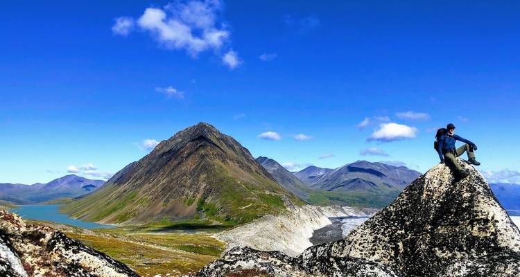 Persoon op een rotsachtige top met uitzicht op een bergketen.