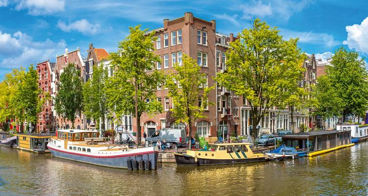 Casas de canal de ladrillo clásicas, árboles frondosos y casas flotantes a lo largo de un canal soleado de Ámsterdam