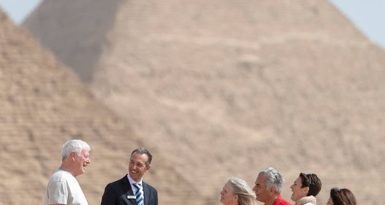 Un groupe de touristes discute devant les pyramides lointaines de Giza lors d'une matinée désertique brumeuse.