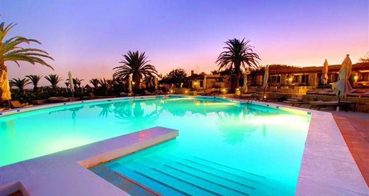 Piscine de luxe entourée de palmiers au coucher du soleil.