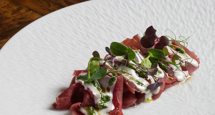 Angerichtetes Rindfleisch-Carpaccio mit Mikrogrün, cremiger Sauce und Pesto-Drizzle