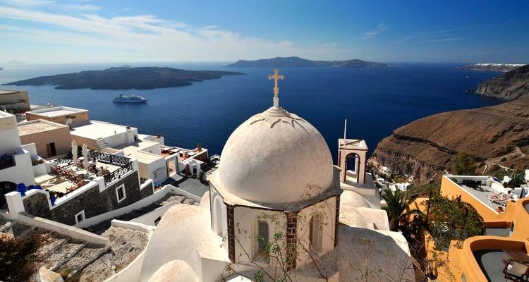 Icónica cúpula encalada y cruz de una iglesia de Santorini con vista a la caldera azul profundo y crucero.