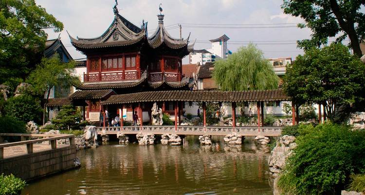 Pavillon chinois traditionnel aux toits courbés ornementés situé près d'un bassin réfléchissant et d'un pont de pierre dans un jardin classique.
