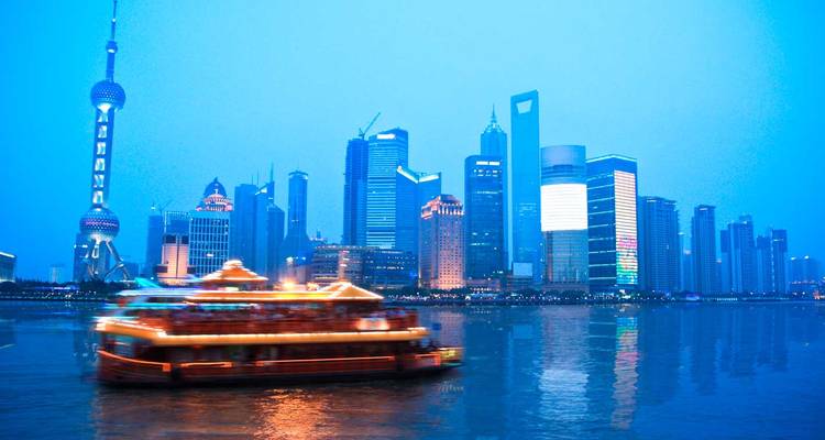 Horizon nocturne de Shanghai avec la Tour de la Perle d'Orient se reflétant sur la rivière Huangpu tandis qu'un bateau de croisière vivement éclairé file à toute vitesse.