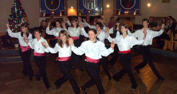 Binnenshuis culturele dansvoorstelling met een rij jonge dansers in witte shirts en rode sjerpen midden in een danspas.