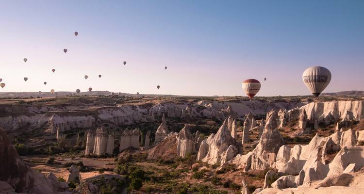 Tientallen heteluchtballonnen drijven bij zonsopgang boven dramatische rotspitten en dalen