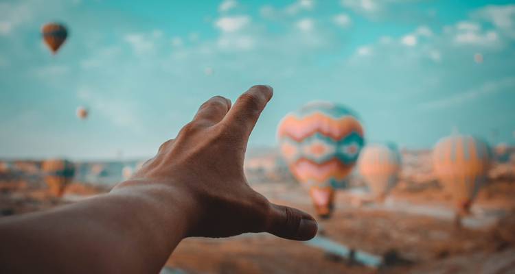 Uitgestrekte hand die naar kleurrijke heteluchtballonnen reikt die boven een droog landschap zweven