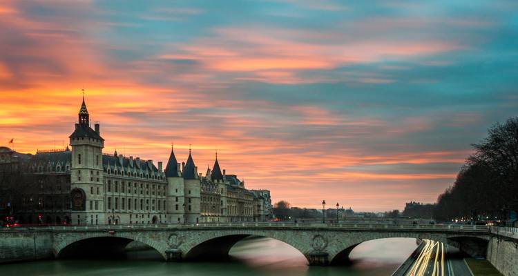 Historic bridge and buildings by a river during sunset.